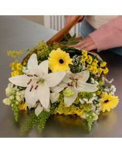 Nærbillede af buket med hvide liljer og gule blomster pakket i brunt papir.