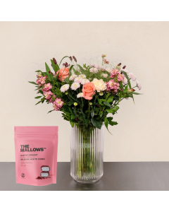 Pastel blomsterbuket med lyserøde roser, lyserøde og hvide blomster i glasvase samt pose med skumfiduser.