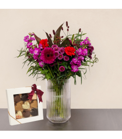 Fødselsdagsbuket med pink og røde blomster i glasvase samt æske med chokolade.