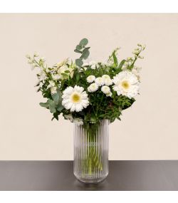Nordisk blomsterbuket med hvide gerbera, hvide blomster og grønt i høj glasvase.