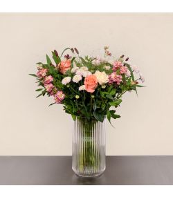 Buket med lyserøde roser, lyserøde og hvide blomster samt grønt i høj glasvase.