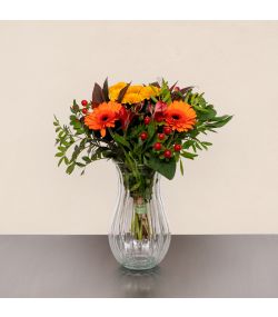 Efterårsbuket med orange gerbera, røde bær, gule blomster og grønt i glasvase.