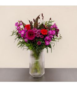 Fødselsdagsbuket med pink og røde blomster samt lilla blomster i høj glasvase.