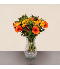 Efterårsbuket med orange gerbera, røde bær, gule blomster og grønt i glasvase.