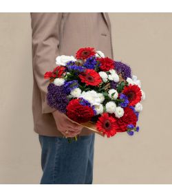 Buket med røde, hvide og lilla blomster pakket i brunt papir.