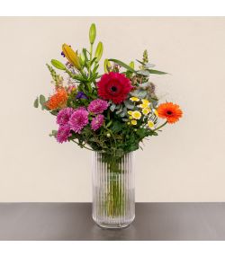 Buket med orange liljer, pink og orange gerbera samt lilla og hvide blomster i glasvase.