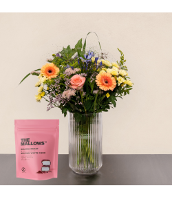 Pastel blomsterbuket med ferskenfarvede gerbera, lyserød rose, blå blomster og pose med skumfiduser.