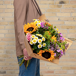 Sommer solsikkebuket med solsikker, floks, limonium, grenede krysantemum og roser bundet med pistache og hareøre – en fyldig og sæsonaktuel blomsterbuket, perfekt som gave, sommerhilsen eller blomsterlevering til hjemmet.