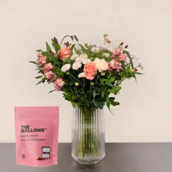 Pastel blomsterbuket med lyserøde roser, lyserøde og hvide blomster i glasvase samt pose med skumfiduser.