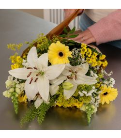 Nærbillede af buket med hvide liljer og gule blomster pakket i brunt papir.